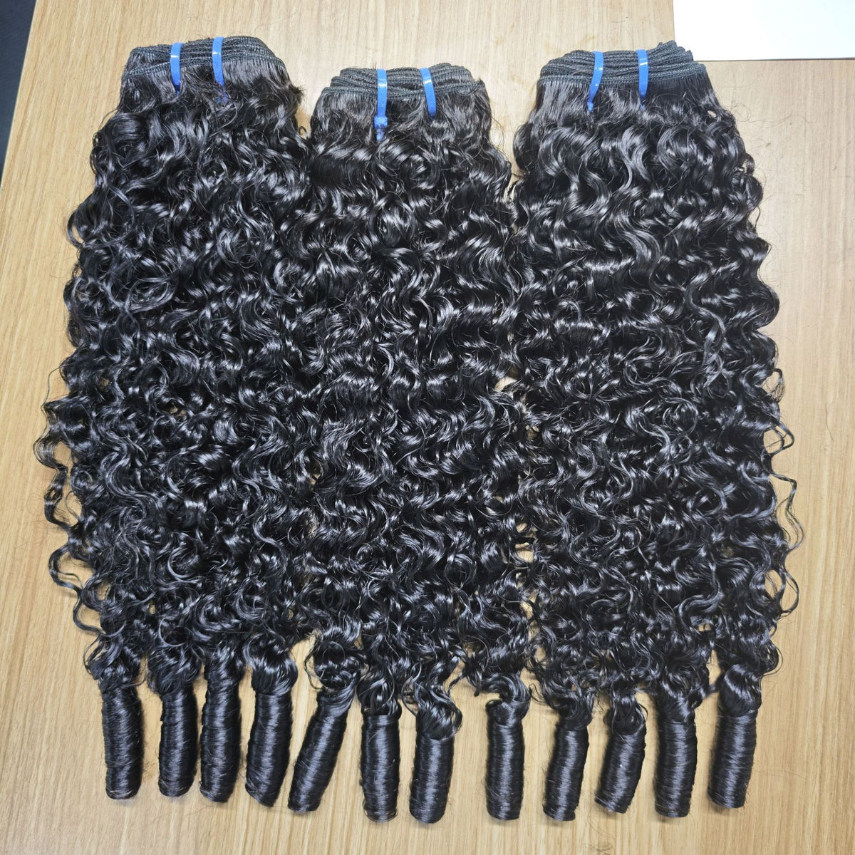 Three bouncy curly natural black hair bundles laid flat